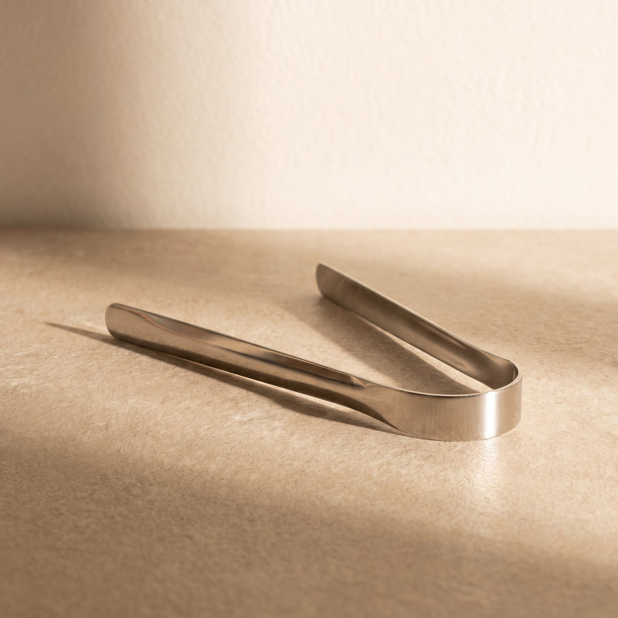 Stainless-steel OralCove tongue scraper resting diagonally on a warm neutral surface.