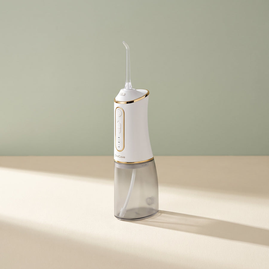 White OralCove portable oral irrigator shown at a three-quarter angle on a warm ivory surface.